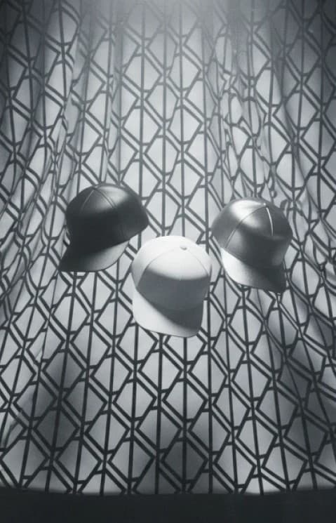 Three caps floating over the interlocking brand pattern, in black and white